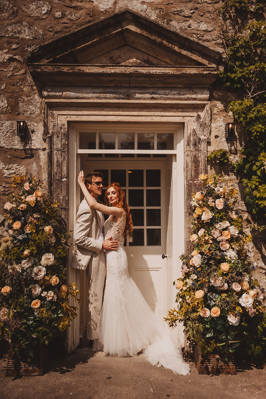 Wedding couple posing at the flower-framed entrance of Broomholm Manor during a luxury Scottish wedding.