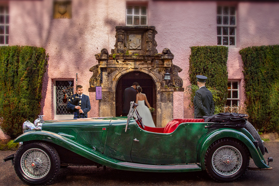 Newlyweds enter Thackray House as a piper performs beside a vintage green wedding car.