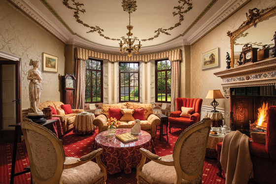 Historic lounge at Thackray House with ornate fireplace, period furniture, bay windows and classical statue.