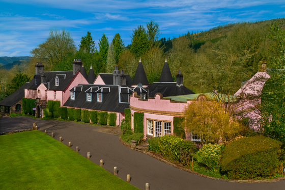 Exterior of Thackray House showing its distinctive pink walls, turrets, gardens and green lawn.