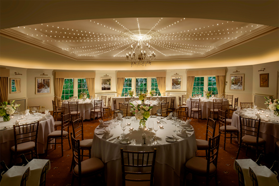 Thackray House wedding reception room set with round tables, floral centrepieces, Chiavari chairs and ceiling lights.