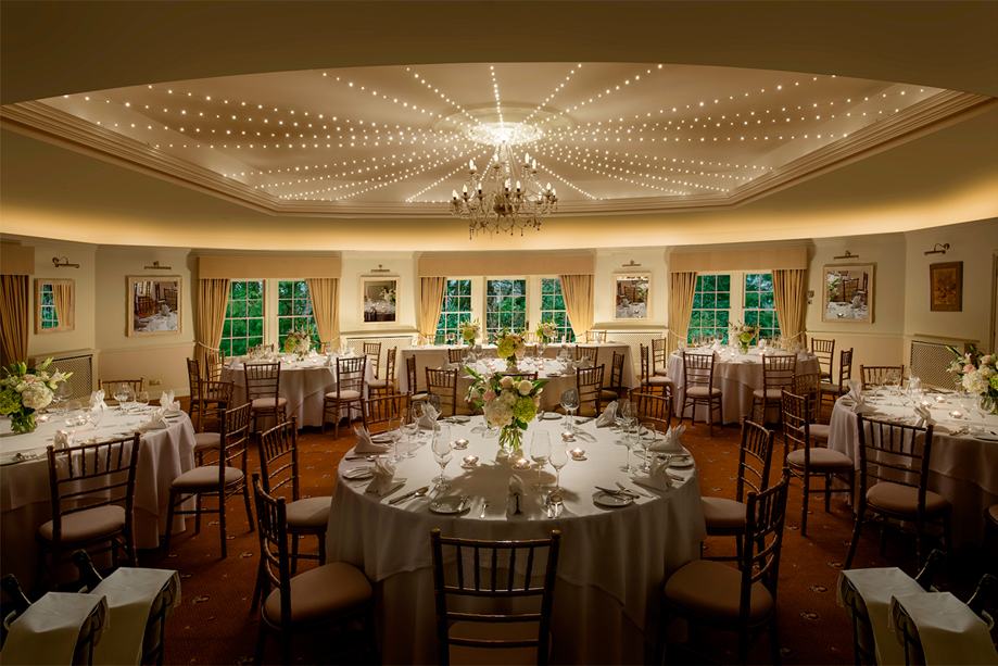 Thackray House wedding reception room set with round tables, floral centrepieces, Chiavari chairs and ceiling lights.
