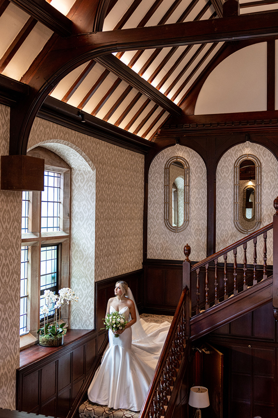 Bride standing on the staircase at Piersland House holding a bouquet and looking towards the window