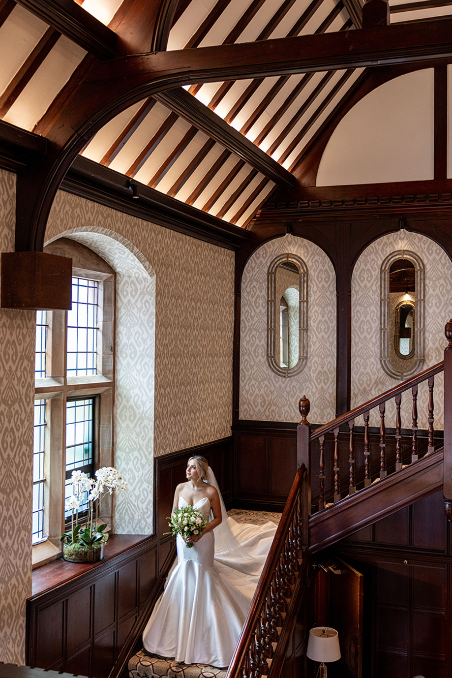 Bride standing on the staircase at Piersland House holding a bouquet and looking towards the window