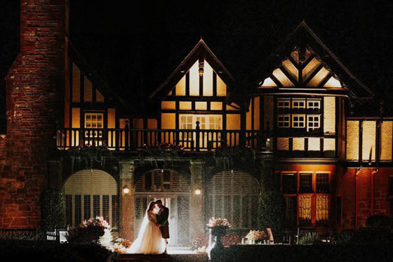 Newlywed couple kissing in the rain on the terrace outside Piersland House at night