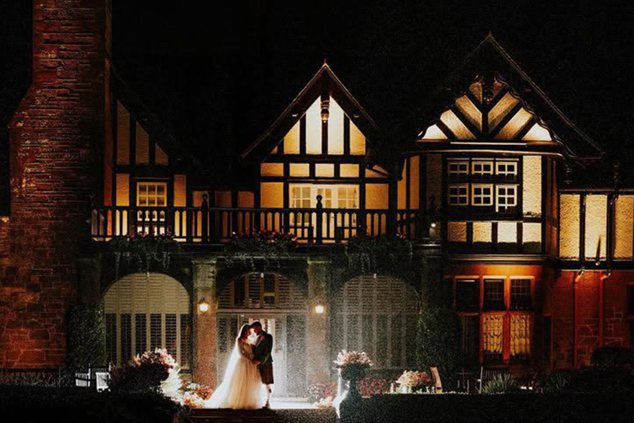 Newlywed couple kissing in the rain on the terrace outside Piersland House at night