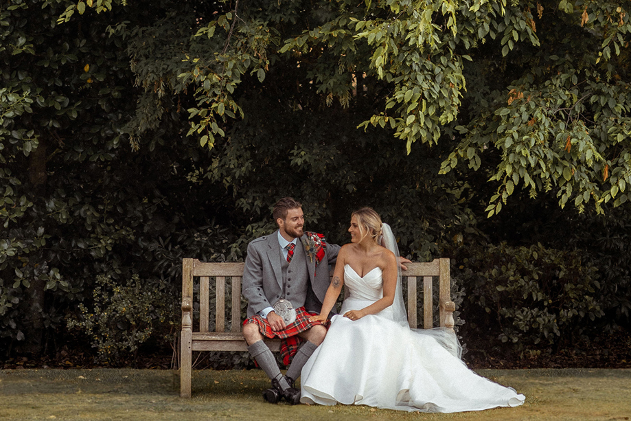 Newlywed couple sitting together on a wooden garden bench at Piersland House wedding venue