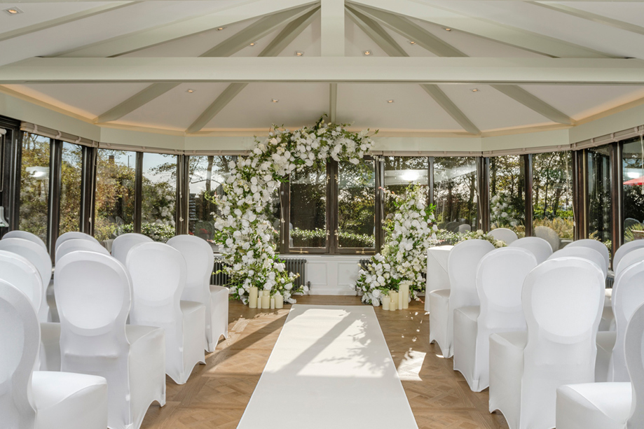 Piersland House wedding ceremony setup with white chairs, aisle runner and large white floral arch