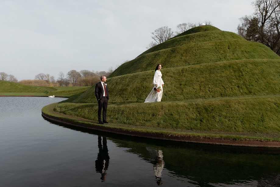 Bride and groom beside the sculpted grassy landforms and water at Jupiter Artland in West Lothian