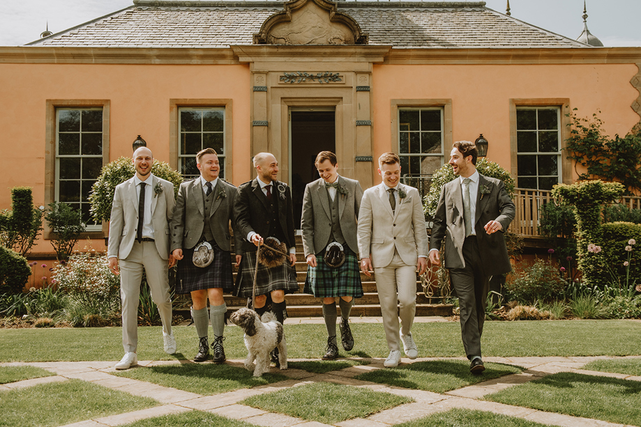 Groom and groomsmen walking with a dog through the gardens at Jupiter Artland wedding venue