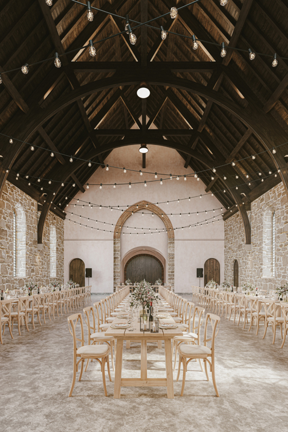 Grand Hall at The West Works Glasgow set for a wedding breakfast, with long wooden tables, floral centrepieces and festoon lighting