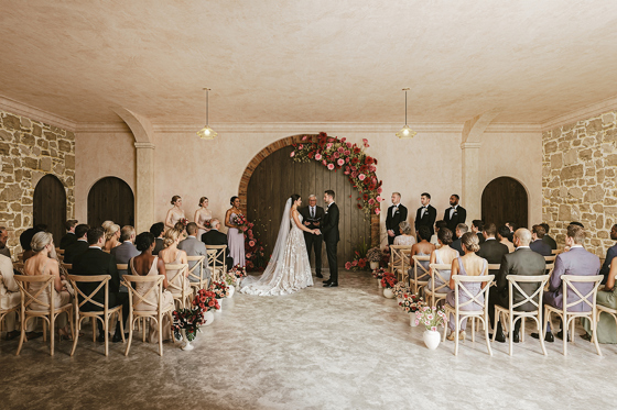 Wedding ceremony underway in the Garden Room at The West Works Glasgow, with bride and groom beneath a red and pink floral arch