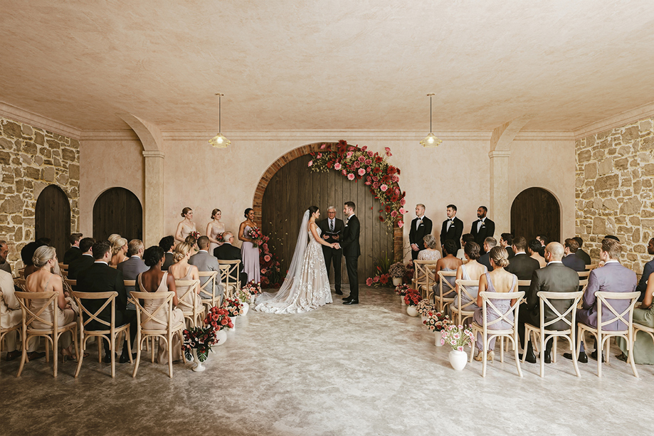 Wedding ceremony underway in the Garden Room at The West Works Glasgow, with bride and groom beneath a red and pink floral arch