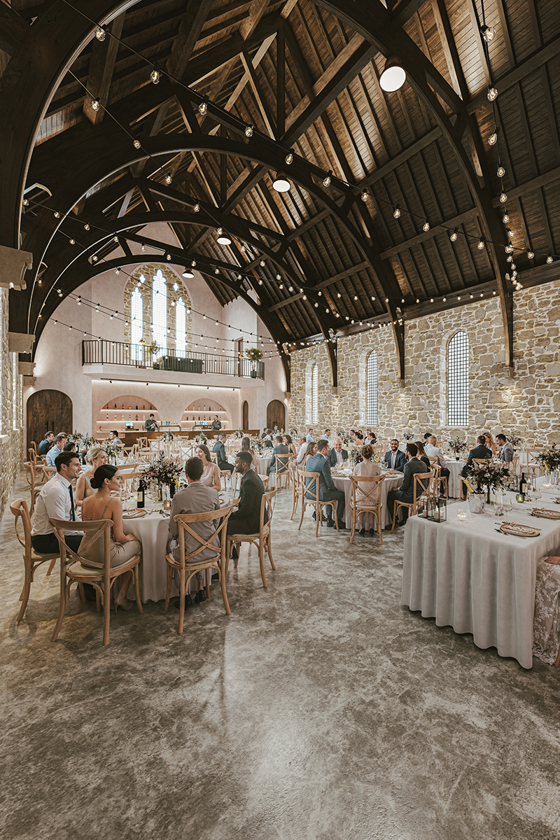 1. Wedding breakfast in the Grand Hall at The West Works Glasgow, with guests seated beneath curved timber beams and festoon lights