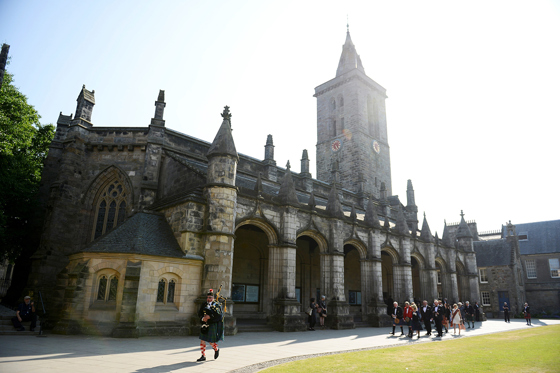 Traditional Scottish bagpiper leads a wedding party past the historic St Salvator's Chapel at the University of St Andrews.