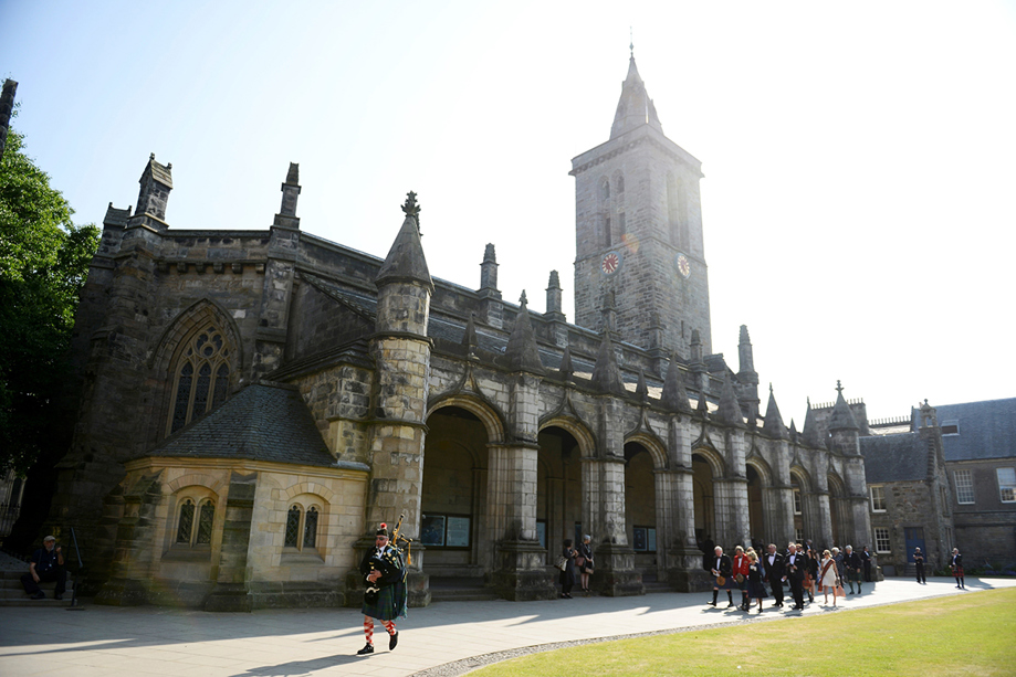 Traditional Scottish bagpiper leads a wedding party past the historic St Salvator's Chapel at the University of St Andrews.