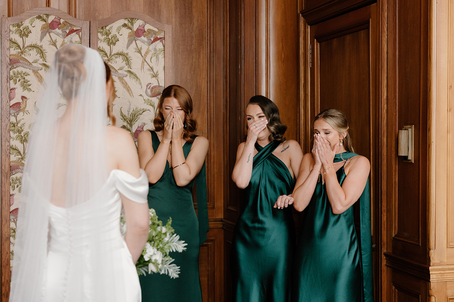 Bridesmaids in dark green dresses react emotionally to seeing the bride at The Edinburgh Grand wedding.