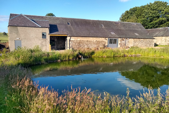 Restored barn at Cormiston Farm reflected in a pond on a sunny day in the Clyde Valley