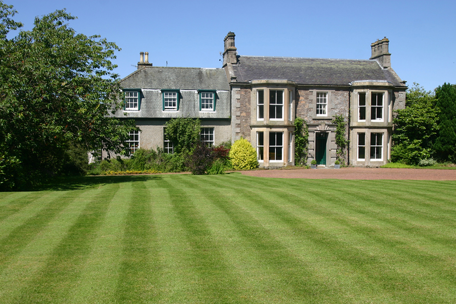 Cormiston Farmhouse exterior with manicured lawn and mature trees on a bright summer day