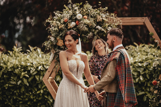 Bride smiles at guests whilst at altar with groom and celebrant smiling in background