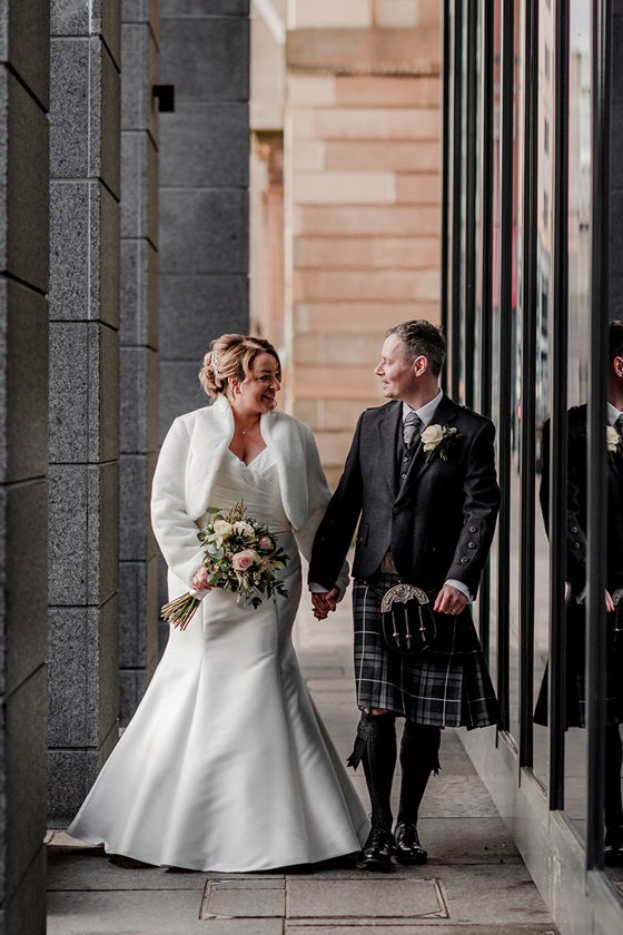 Bride and groom outside The Clayton Hotel, holding hands as they walk