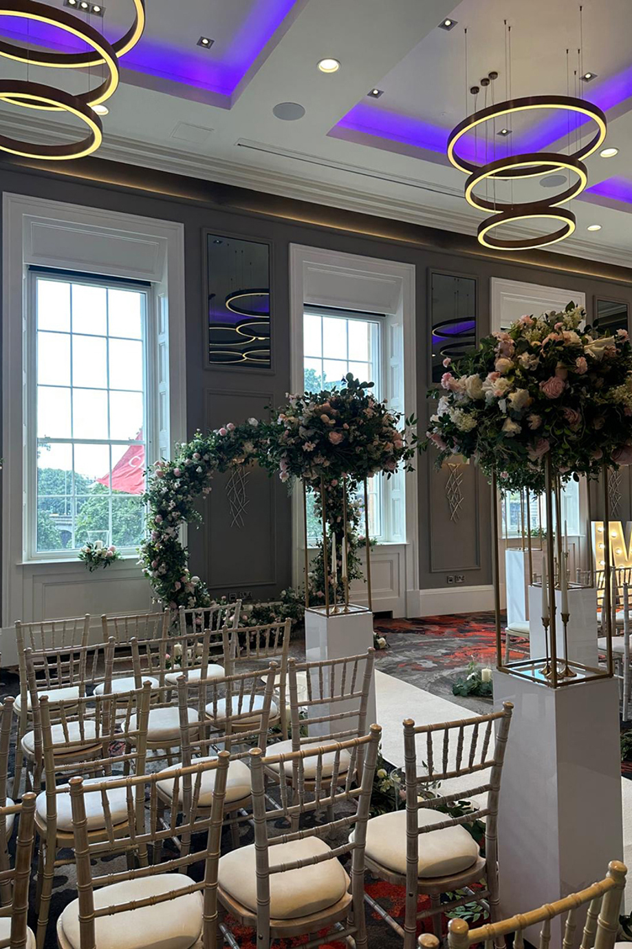 Ceremony set up at Clayton Hotel Glasgow City with gold chiavari chairs, a floral hoop and floral installations on gold stands
