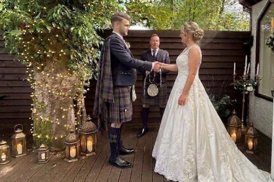 Outdoor wedding ceremony at Dalgarven House with bride, groom in kilt, celebrant and lantern-lit decking