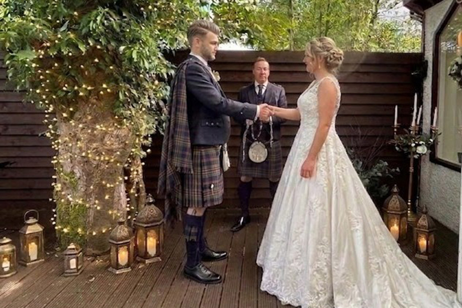 Outdoor wedding ceremony at Dalgarven House with bride, groom in kilt, celebrant and lantern-lit decking