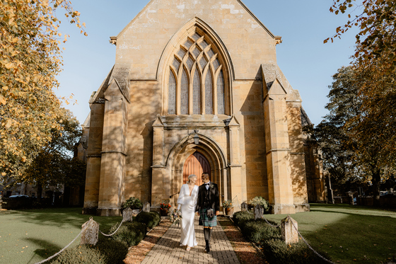 Newly married couple walking hand in hand outside historic cathedral near Dornoch Station Hotel wedding venue