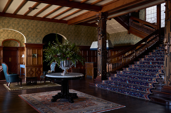 Grand lobby at Dornoch Station Hotel featuring dark wood staircase, patterned carpet and floral centrepiece table