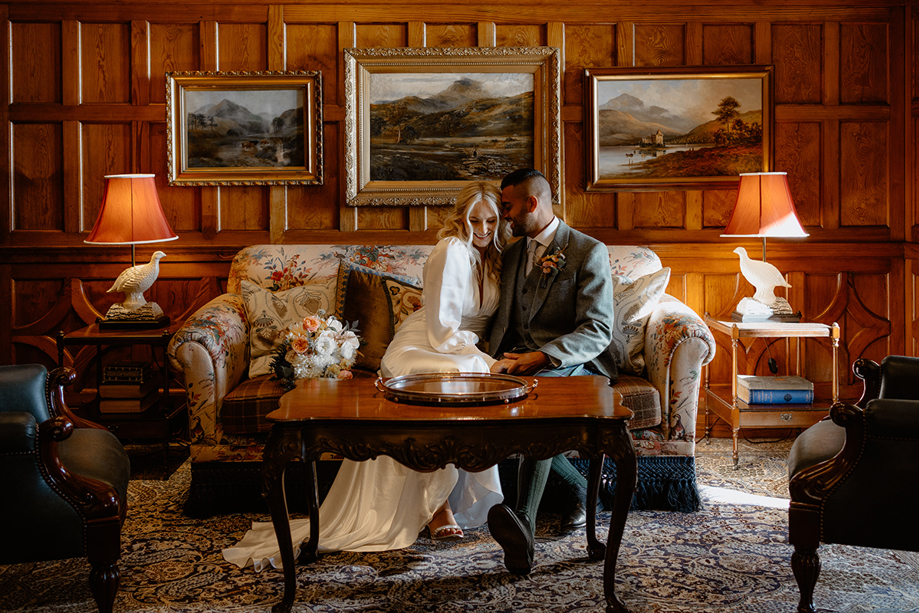 Bride and groom sitting together on sofa in wood-panelled lounge at Dornoch Station Hotel wedding venue