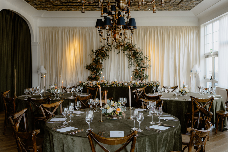 Wedding reception tables at Dornoch Station Hotel with green velvet linens, floral centrepieces and top table floral arch