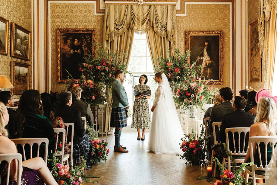 Indoor wedding ceremony at Drumtochty Castle held in an elegant historic room with floral arch and seated guests.