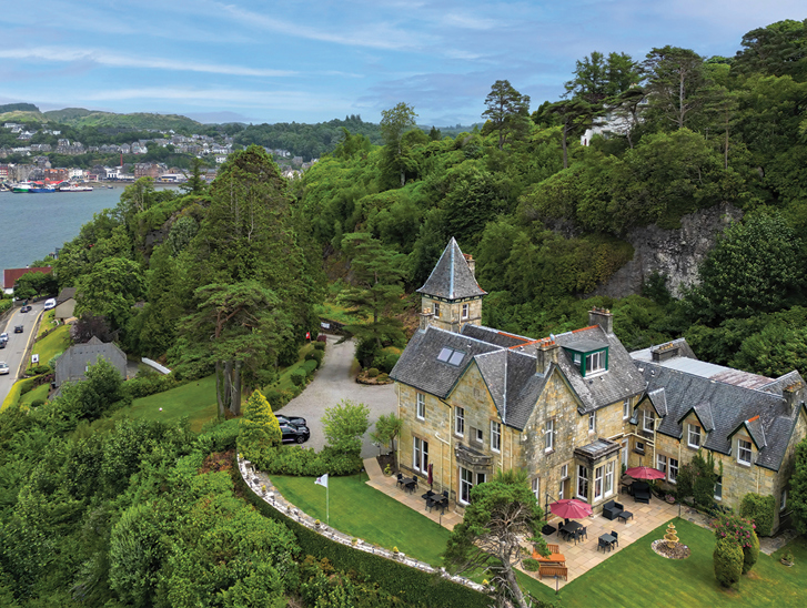 External view of Dungallan Country House in Argyll and Bute, with views of the sea and hills in background and trees behind venue.