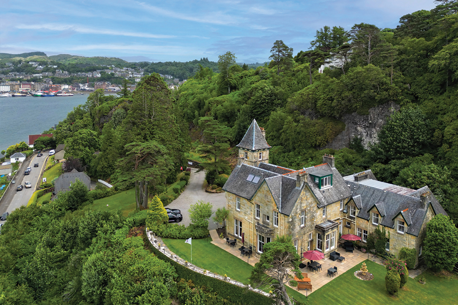 External view of Dungallan Country House in Argyll and Bute, with views of the sea and hills in background and trees behind venue.