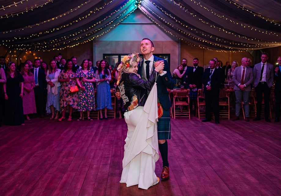 Bride wearing flower crown and leather jacket has first dance with her groom