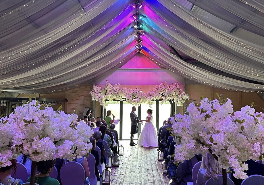 Bride and groom at the altar with draped, multicolour ceiling above them and flowers in foreground