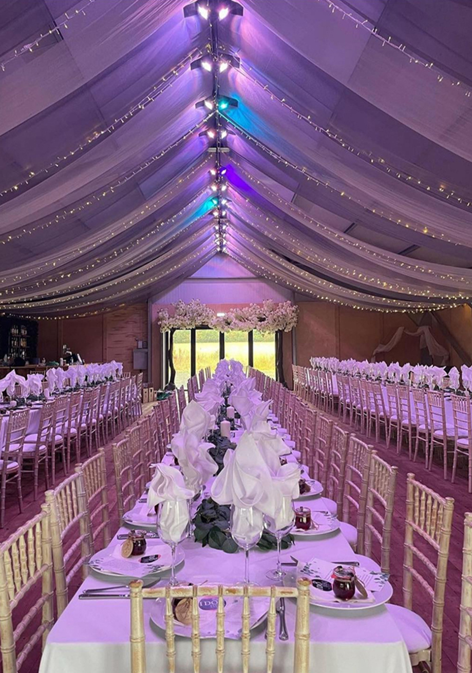 Portrait image of long tables for a wedding meal with multicoloured draped ceiling