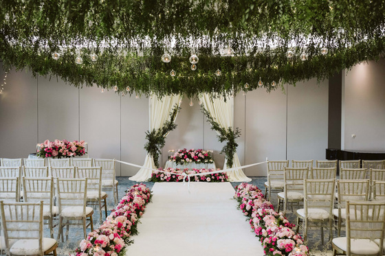 Pink flowers line each side of the aisle with greenery draping from ceiling