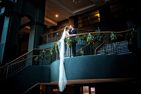 Brides veil drapes over bannister of stunning leaf decorated staircase as bride and groom kiss