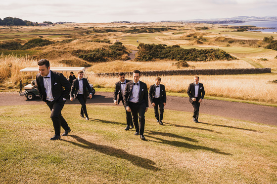 Groomsmen walk up hill together with golf cart in background
