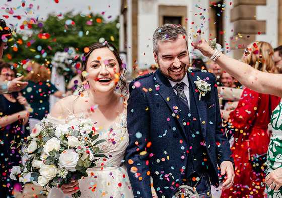 Bride and groom smile as they walk out of ceremony to confetti