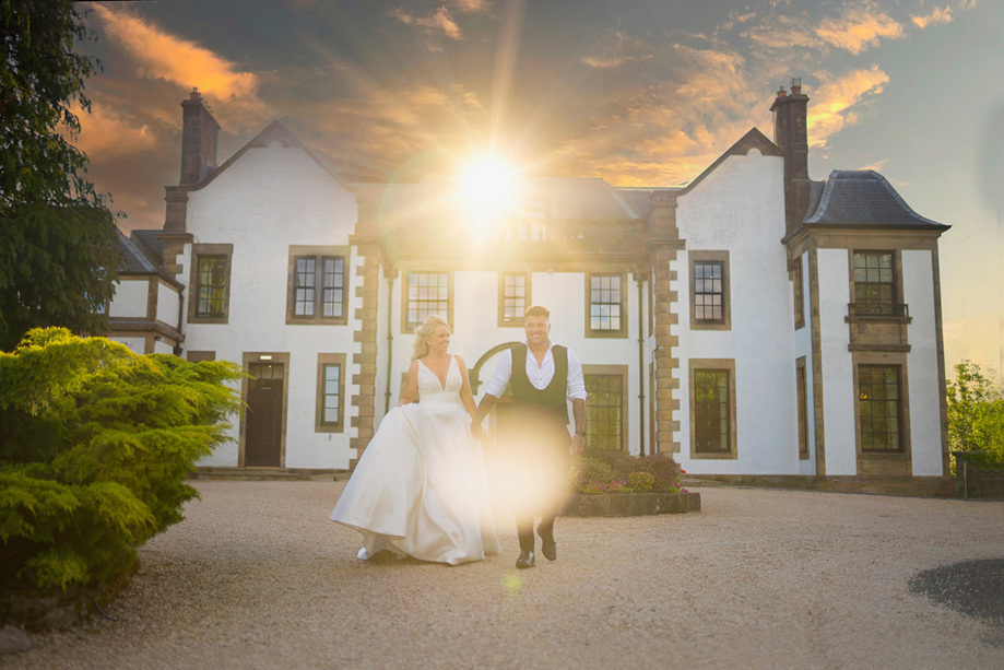 Bride and groom smile and hold hands at sunset outside venue