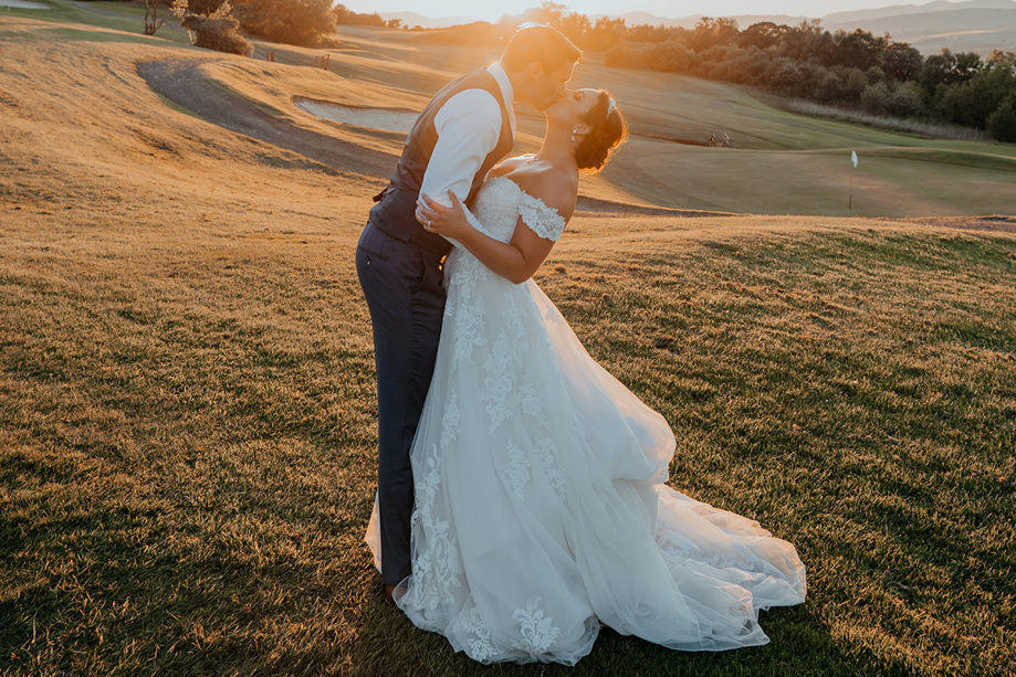 Bride and groom kiss at sunset on the golf course