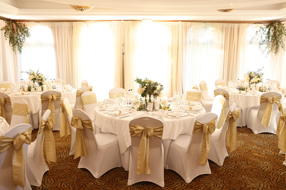 Wedding meal set up with gold bows on chairs and cream rose bouquet centrepieces on tables