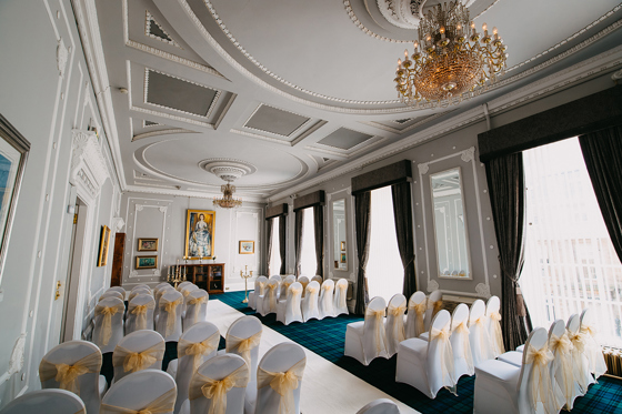 Ornate ceremony room with golden sheer organza bows on chairs