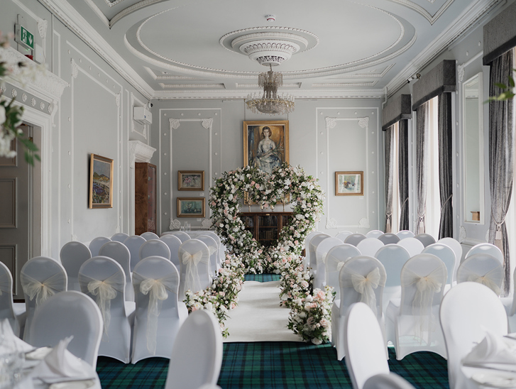 Ceremony set up for photoshoot at 1599 at the Royal College in Glasgow, with white chair covers and cream chiffon bows, and pink and white flowers lining the aisle to a large love heart shaped floral arch at the altar.