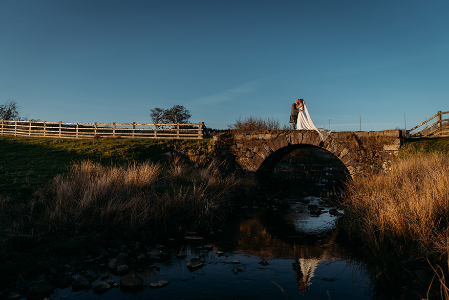 Bride and groom pose on stone bridge at Ayrshire wedding venue, Harelaw Farm