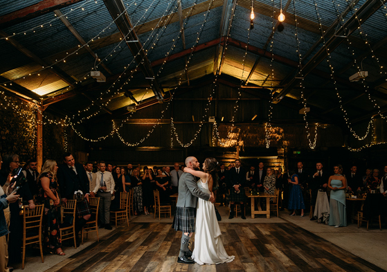 Bride and groom's first dance at Harelaw Farm in Ayrshire, beneath draped fairy lights and guests watching on in background.