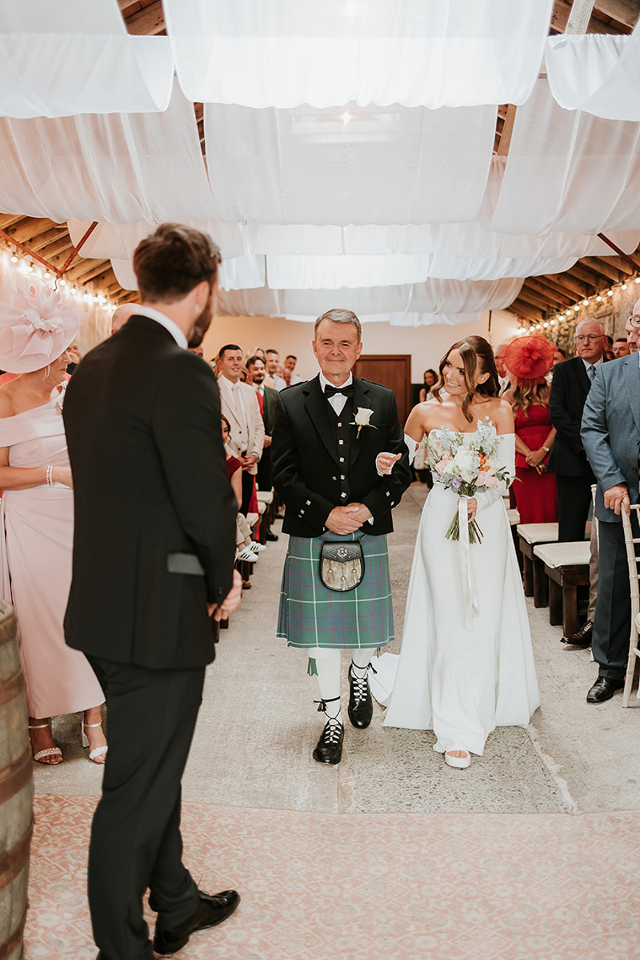Bride smiles at her mother as her father walks her to the altar.